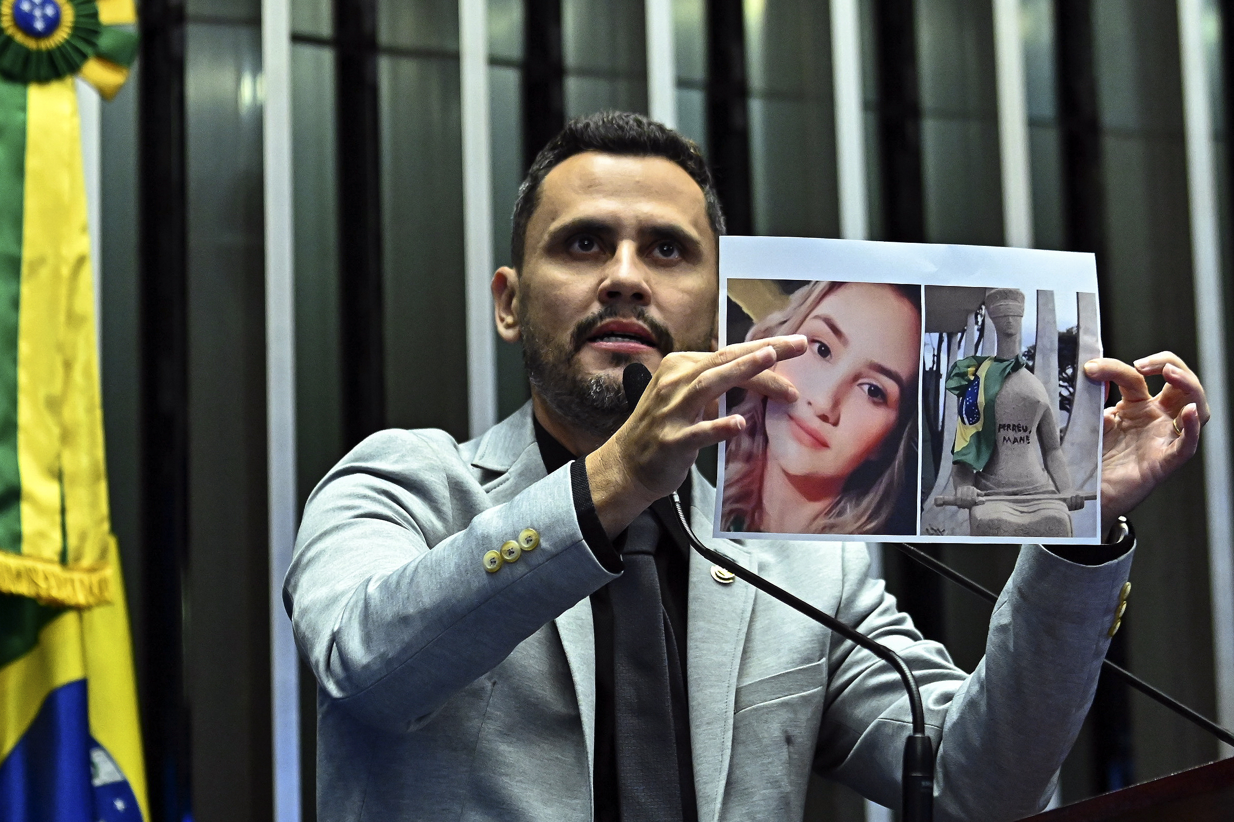 Cleitinho, de terno cinza claro, discursa ao microfone na tribuna do Senado segurando uma imagem com as duas mãos