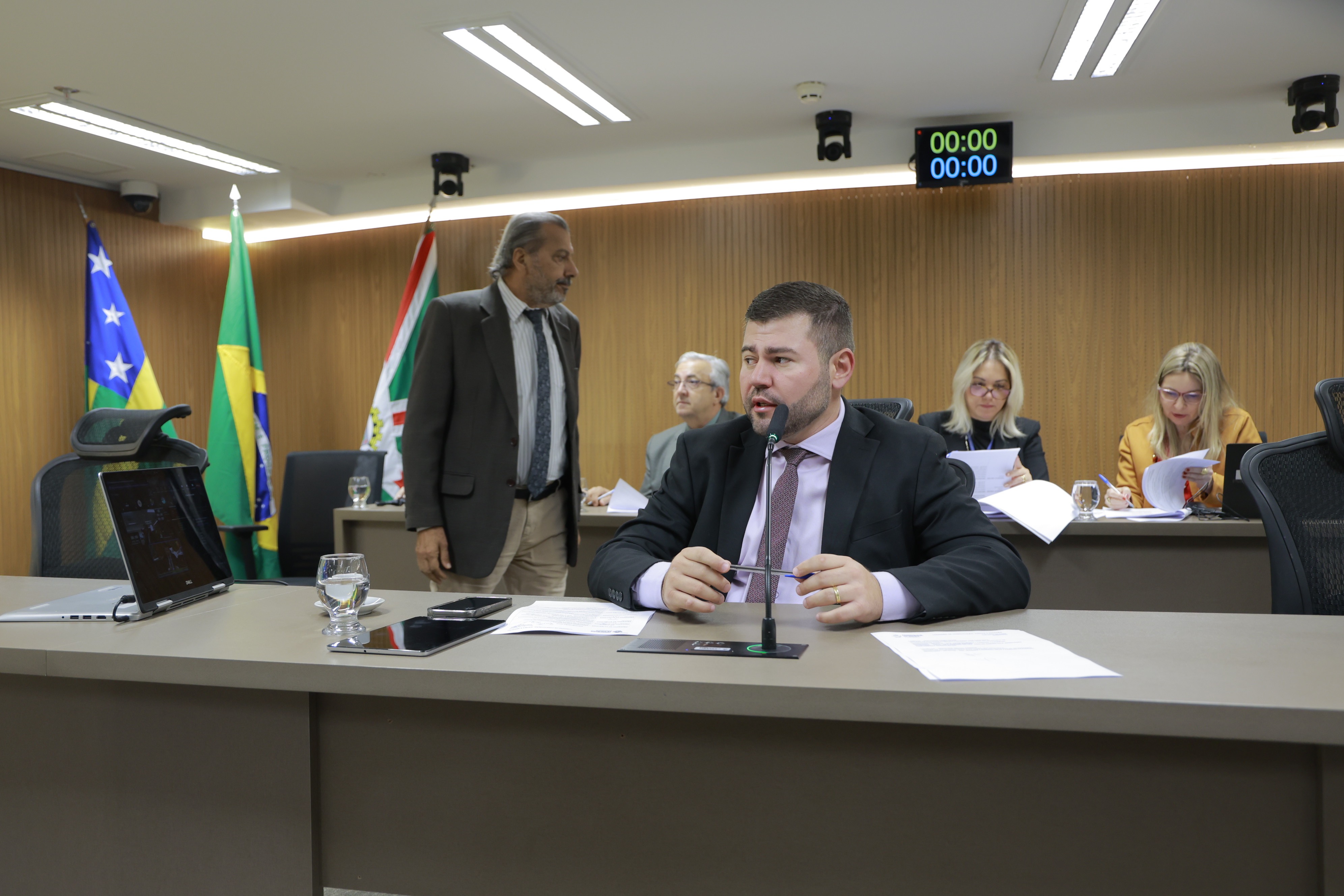 Parlamentares reunidos na mesa da Comissão de Constituição, Justiça e Redação da Alego, com bandeiras de Goiás e do Brasil ao fundo