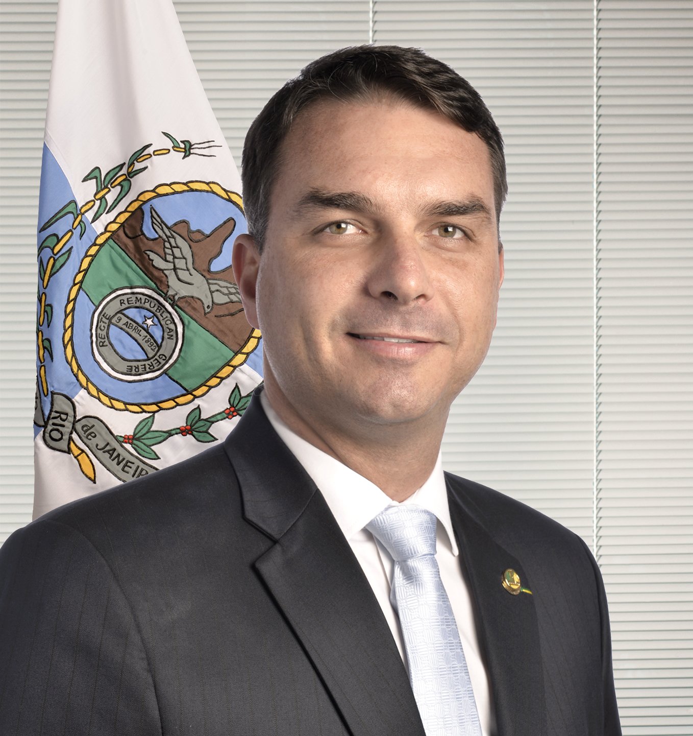 Flávio Bolsonaro em retrato oficial, de terno escuro e gravata clara, diante da bandeira do Rio de Janeiro