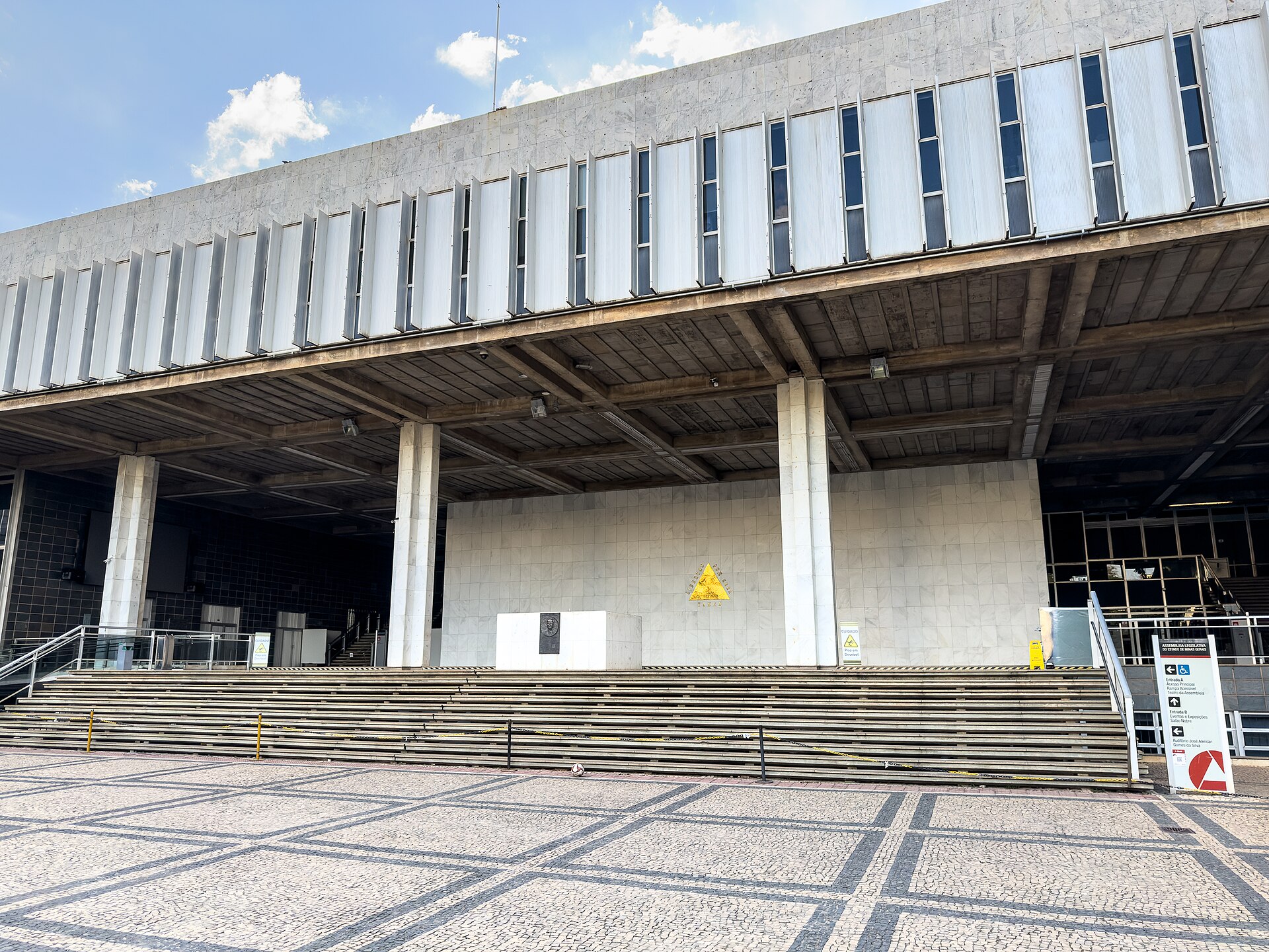 Entrada principal do Palácio da Inconfidência, com escadaria, pilotis e o símbolo da ALMG na parede