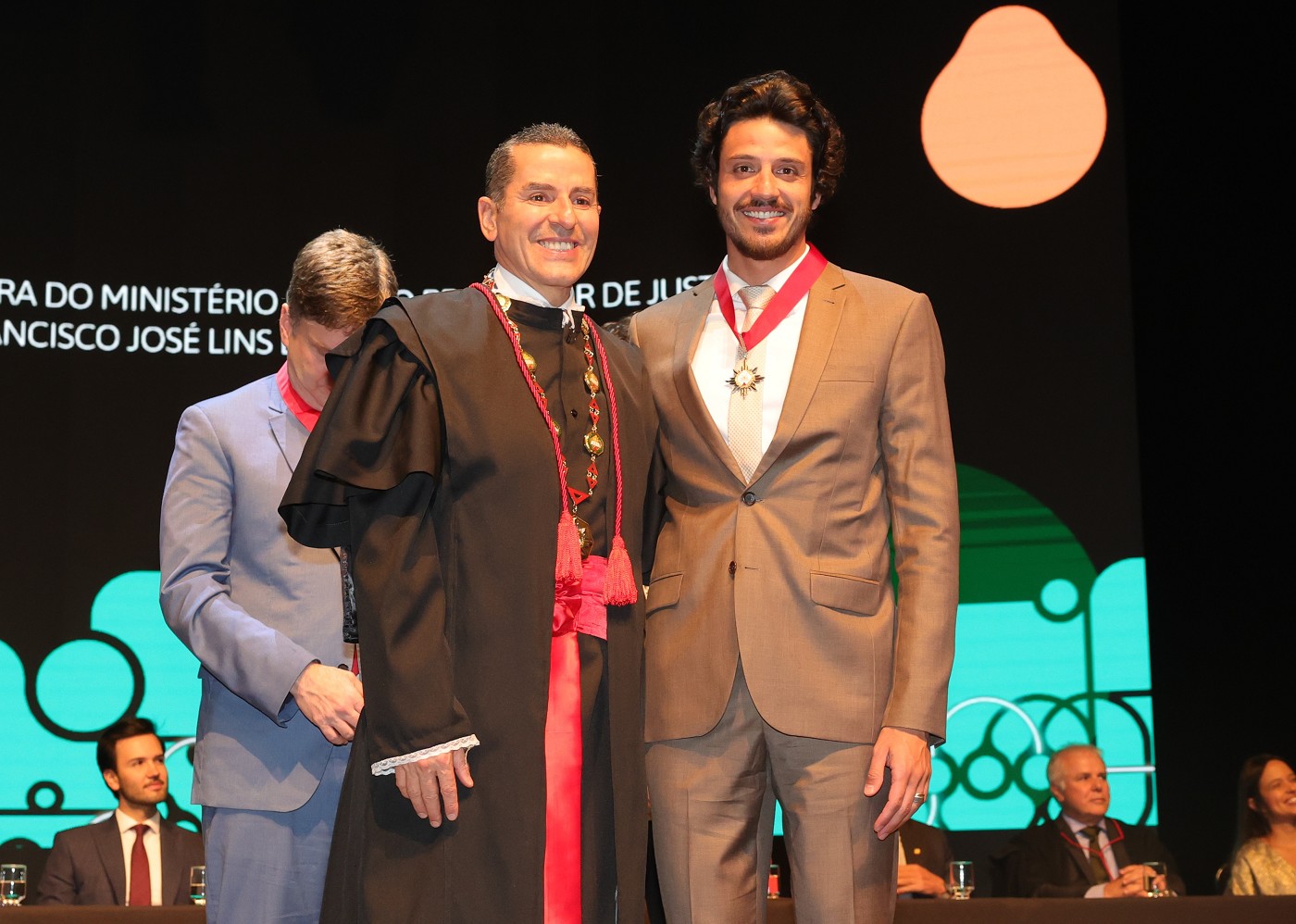 Doorgal Andrada, de terno bege e medalha no peito, sorri em pé ao lado do procurador-geral de Justiça de Minas, vestido de toga