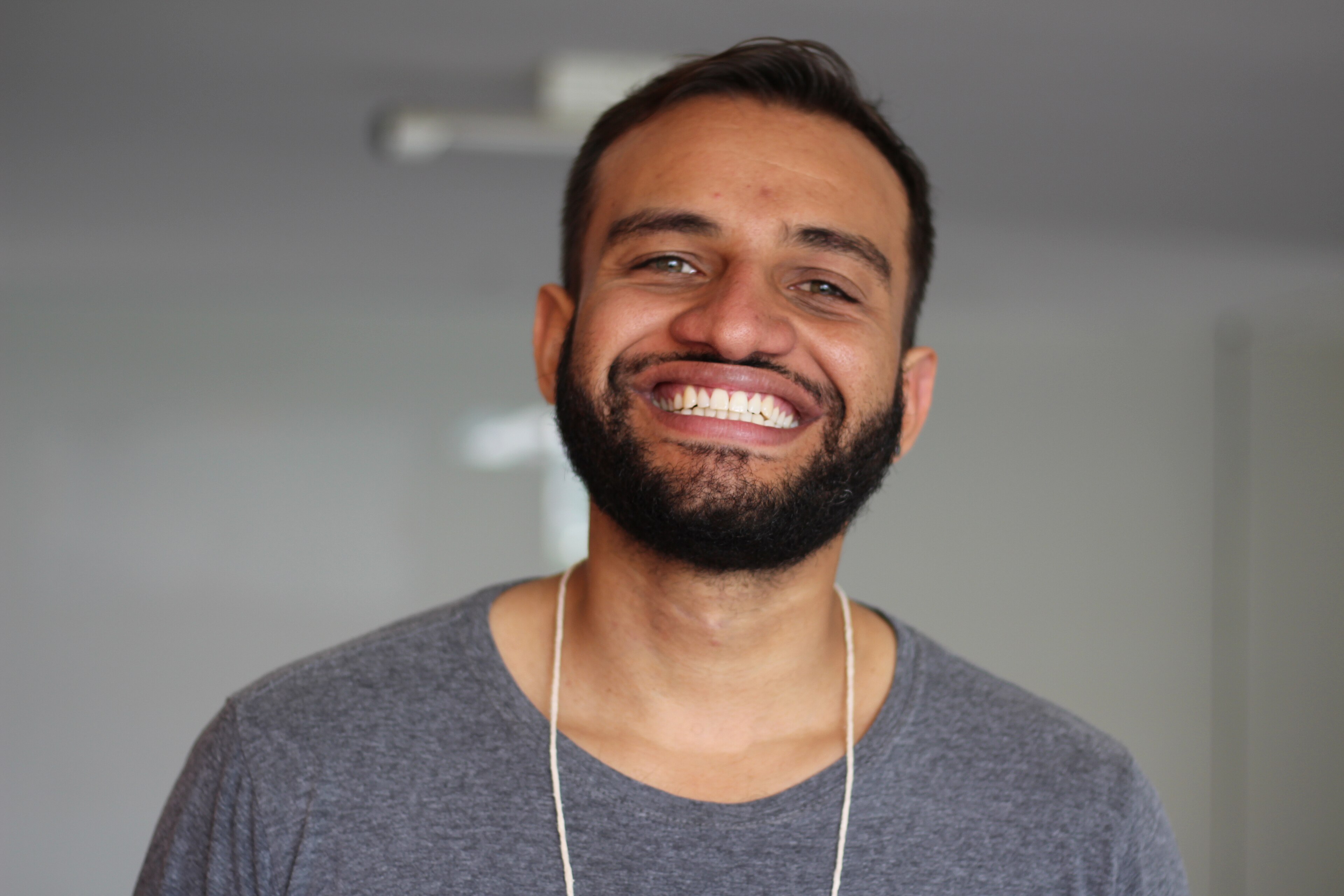 Fábio Felix, de barba e camiseta cinza, sorri abertamente olhando para a câmera